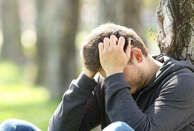 Man sat with head in hands against a tree grieving the loss of his mother