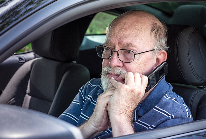 Elderly worried man sat in a car talking on a phone